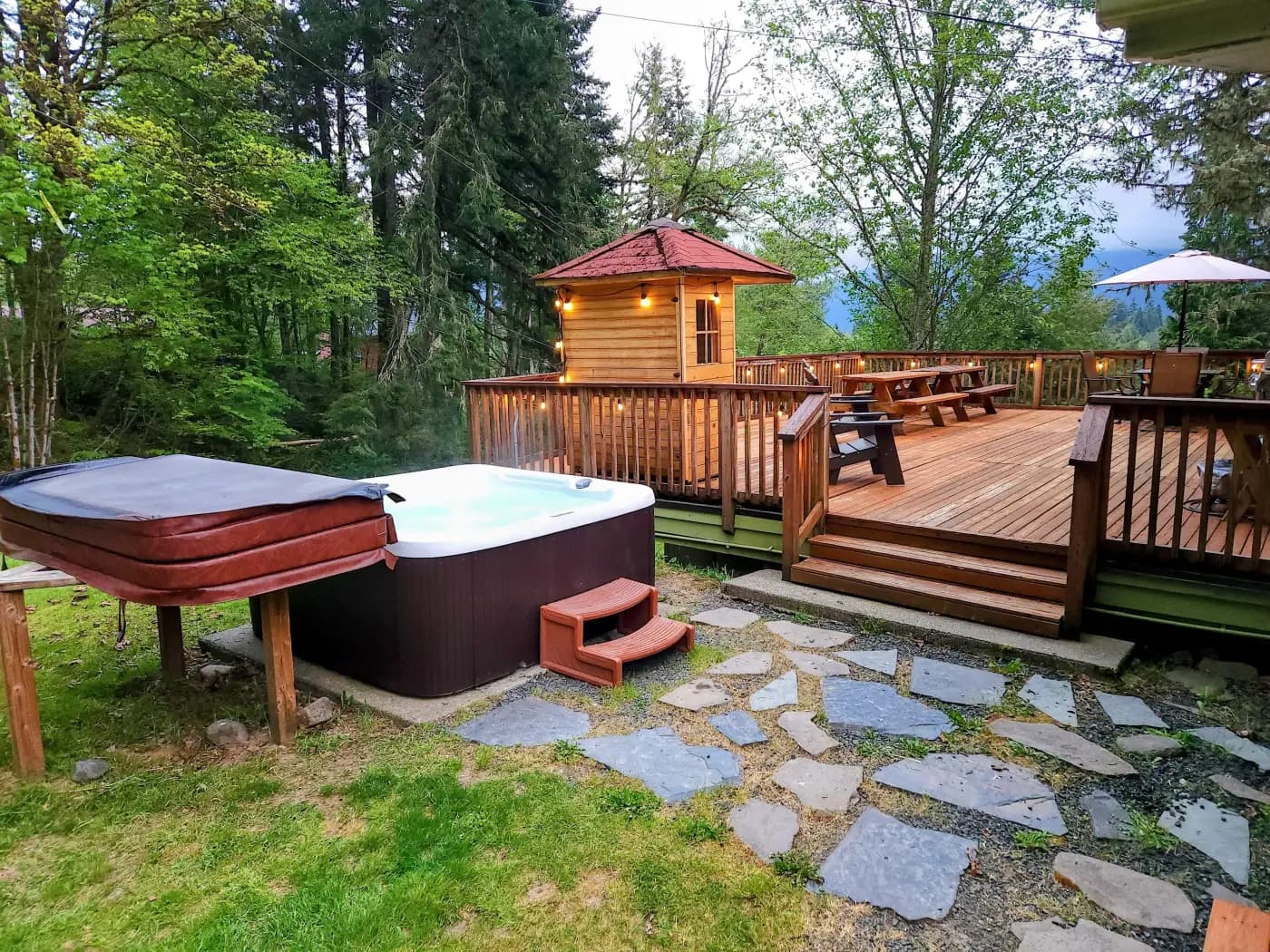 A round hot tub on a wooded deck, with a cabin and mountain view beyond